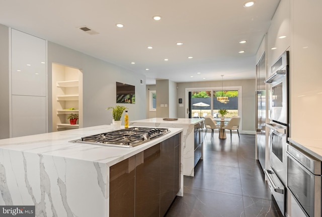 kitchen with stainless steel gas stovetop, white cabinets, hanging light fixtures, light stone countertops, and a large island