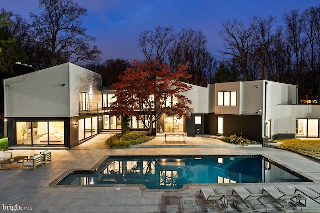 back house at dusk featuring a patio and a balcony