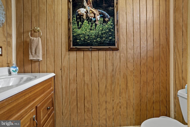 bathroom with vanity, wood walls, and toilet