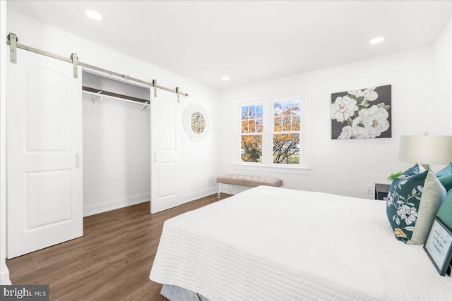 bedroom with a barn door, dark wood-type flooring, and a closet