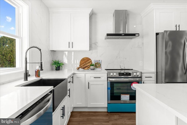 kitchen with wall chimney exhaust hood, dark wood-type flooring, stainless steel appliances, light stone counters, and white cabinets