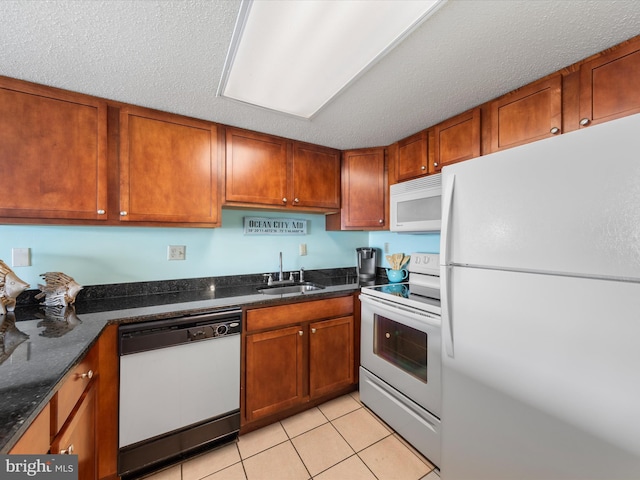 kitchen with sink, dark stone countertops, a textured ceiling, white appliances, and light tile patterned floors