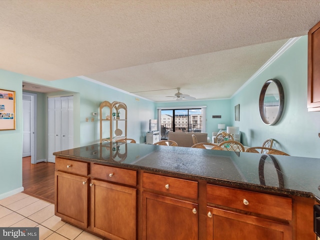 kitchen with dark stone counters, ceiling fan, light tile patterned floors, a textured ceiling, and ornamental molding