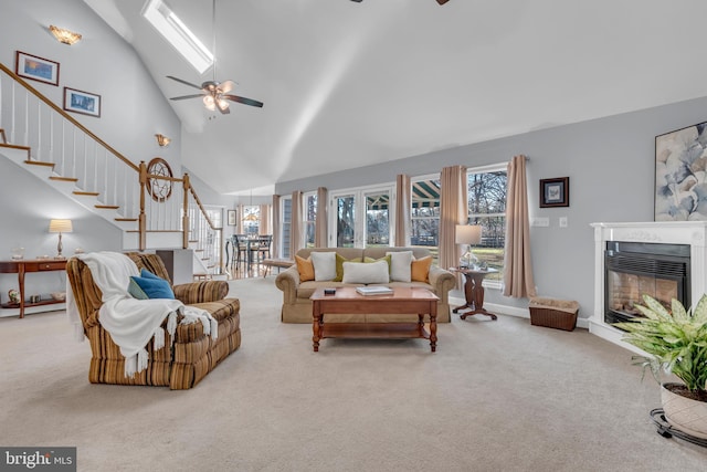 carpeted living room with ceiling fan, high vaulted ceiling, and a skylight