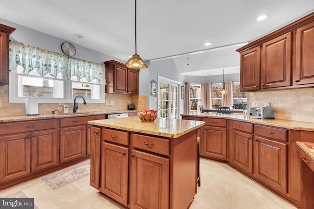 kitchen featuring a center island, sink, decorative backsplash, decorative light fixtures, and light stone counters