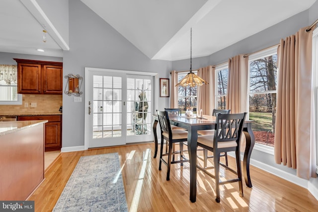 dining room with plenty of natural light, light wood-type flooring, high vaulted ceiling, and a chandelier