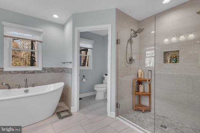 bathroom featuring plus walk in shower, tile patterned floors, toilet, and tile walls