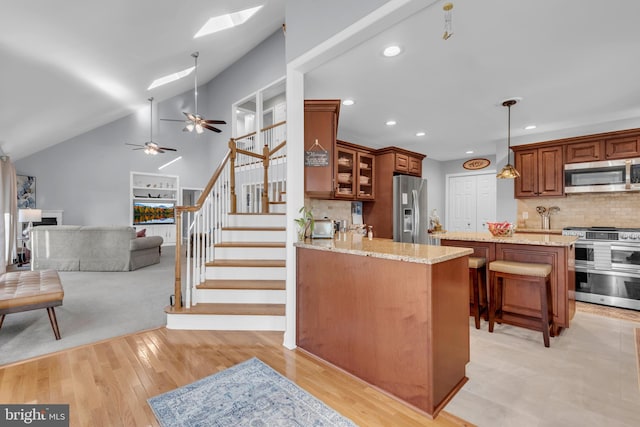 kitchen featuring backsplash, a kitchen bar, vaulted ceiling with skylight, appliances with stainless steel finishes, and light wood-type flooring