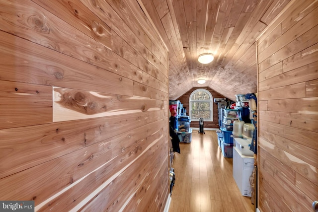 hallway featuring wood walls, light wood-type flooring, and lofted ceiling