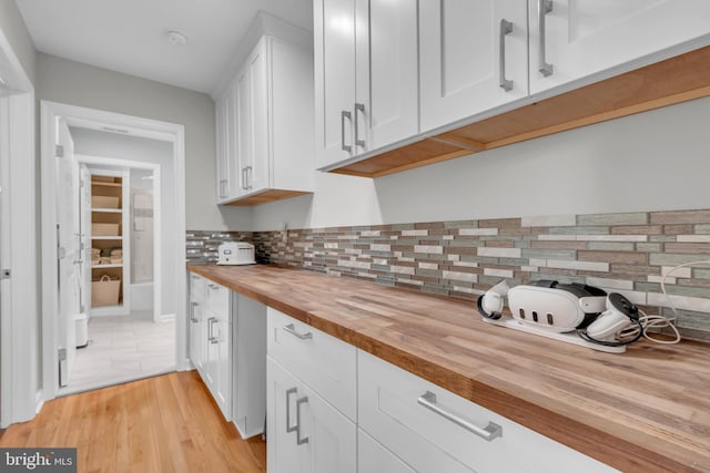 kitchen featuring butcher block countertops, light hardwood / wood-style floors, white cabinetry, and tasteful backsplash