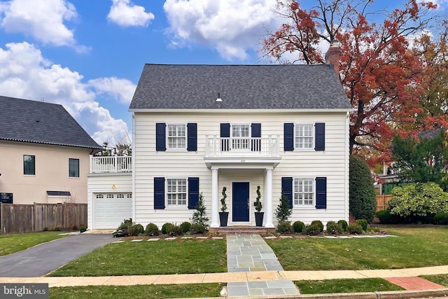 colonial inspired home with a balcony, a garage, and a front lawn