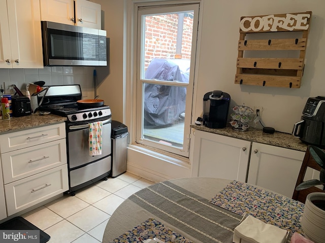 kitchen with white cabinets, light tile patterned floors, appliances with stainless steel finishes, tasteful backsplash, and light stone counters