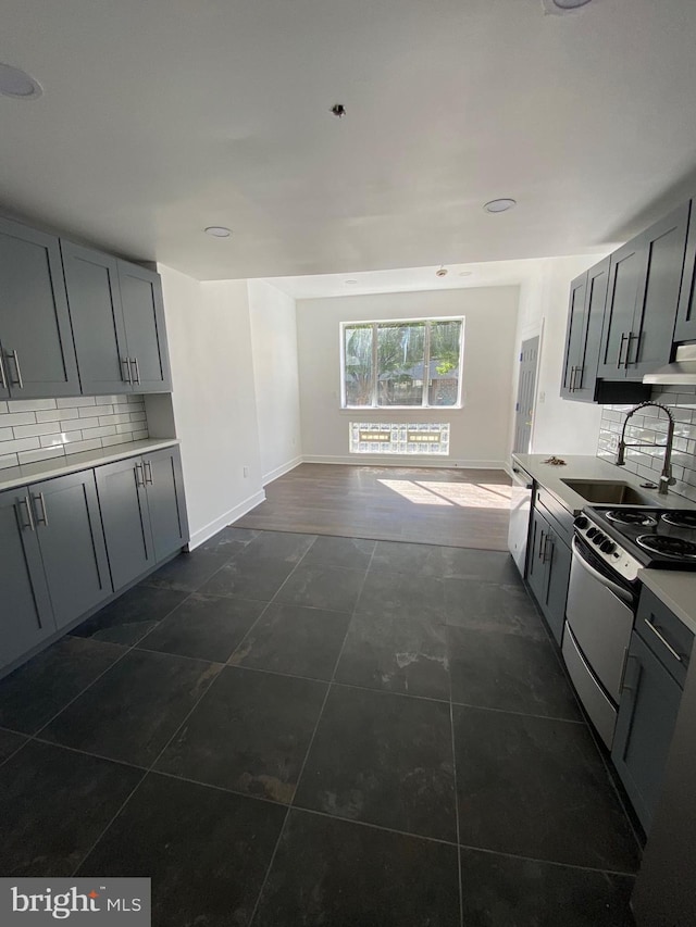 kitchen with stove, backsplash, gray cabinetry, and sink