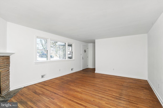 unfurnished living room featuring wood-type flooring and a brick fireplace