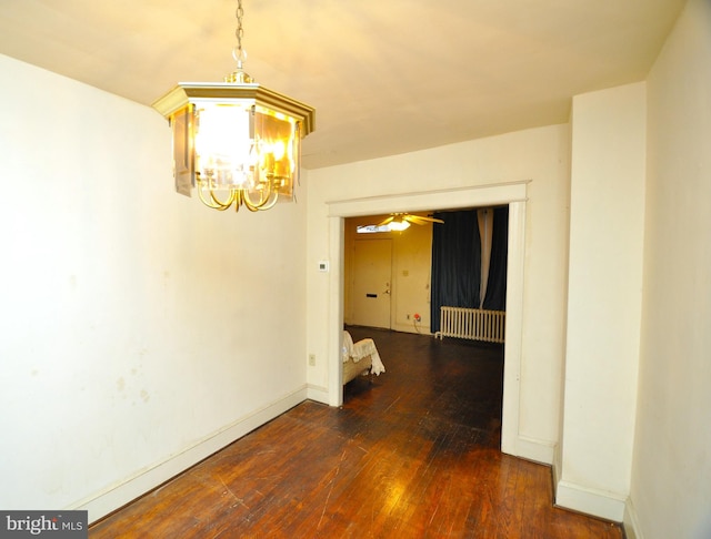 unfurnished dining area with dark hardwood / wood-style floors, radiator heating unit, and ceiling fan with notable chandelier