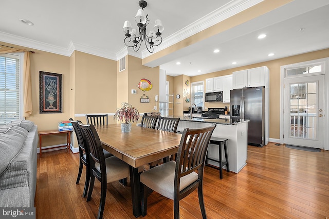 dining area featuring a notable chandelier, light hardwood / wood-style floors, ornamental molding, and sink