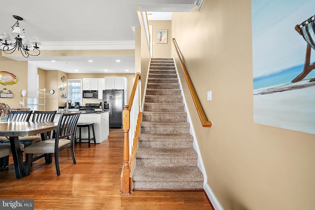 stairs with a notable chandelier, sink, wood-type flooring, and crown molding