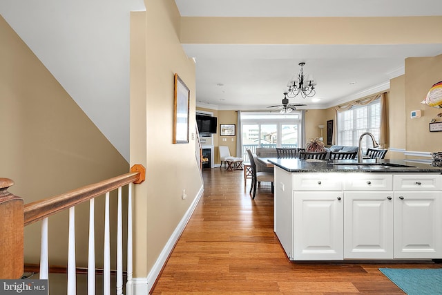 kitchen featuring ceiling fan with notable chandelier, light hardwood / wood-style flooring, white cabinetry, and sink