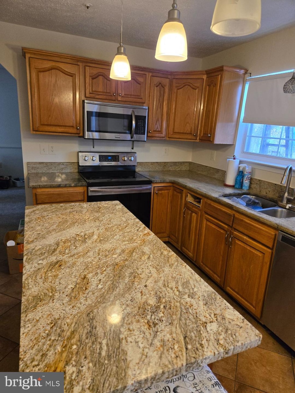 kitchen featuring sink, stainless steel appliances, a textured ceiling, decorative light fixtures, and tile patterned floors