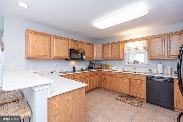 kitchen featuring black appliances, sink, light tile patterned flooring, a kitchen bar, and kitchen peninsula