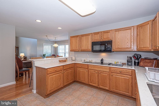 kitchen featuring black appliances, kitchen peninsula, hanging light fixtures, and light hardwood / wood-style flooring