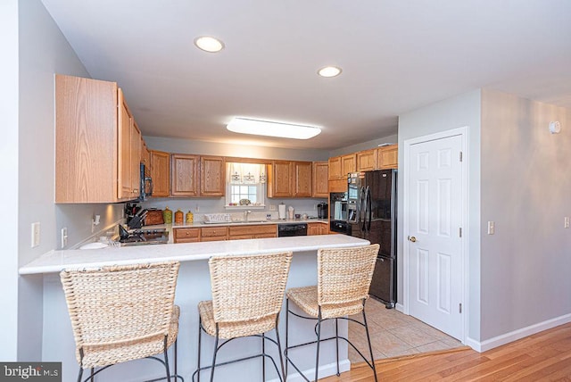 kitchen featuring sink, kitchen peninsula, a breakfast bar area, black appliances, and light wood-type flooring