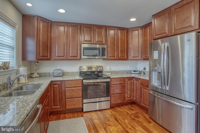 kitchen with light stone countertops, sink, stainless steel appliances, and light wood-type flooring