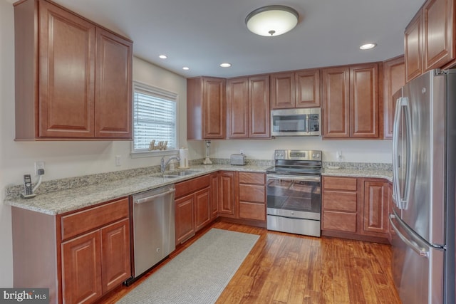 kitchen featuring light stone countertops, light wood-type flooring, sink, and appliances with stainless steel finishes