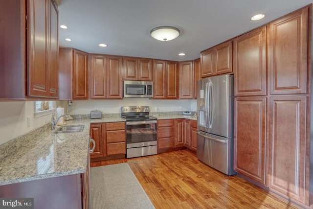 kitchen with light stone countertops, sink, stainless steel appliances, and light hardwood / wood-style floors