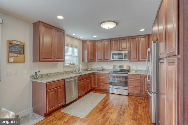 kitchen with light stone countertops, sink, appliances with stainless steel finishes, and light hardwood / wood-style flooring