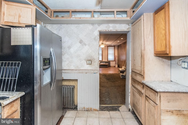 kitchen featuring radiator, ceiling fan, stainless steel fridge, light tile patterned floors, and light stone counters