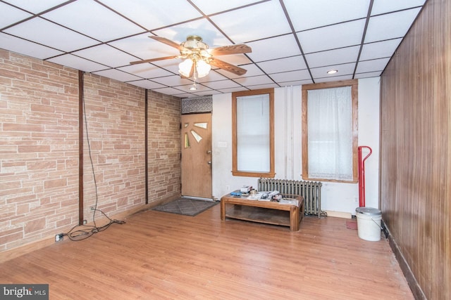 interior space featuring a paneled ceiling, radiator, brick wall, ceiling fan, and light hardwood / wood-style floors