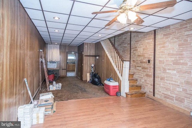 basement featuring wood walls, ceiling fan, brick wall, and hardwood / wood-style flooring