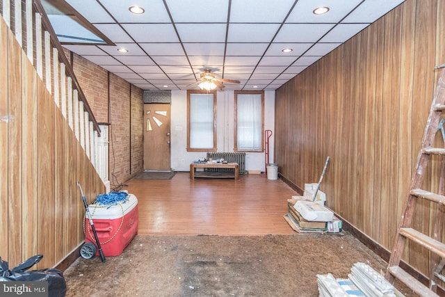 miscellaneous room featuring a paneled ceiling, wooden walls, dark hardwood / wood-style flooring, and ceiling fan