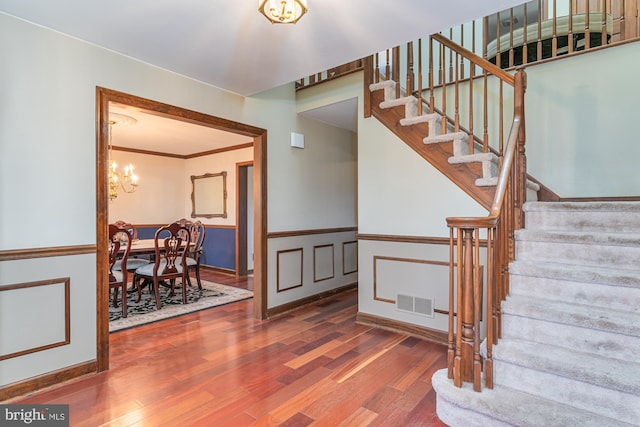 stairs with ornamental molding, a notable chandelier, and hardwood / wood-style flooring