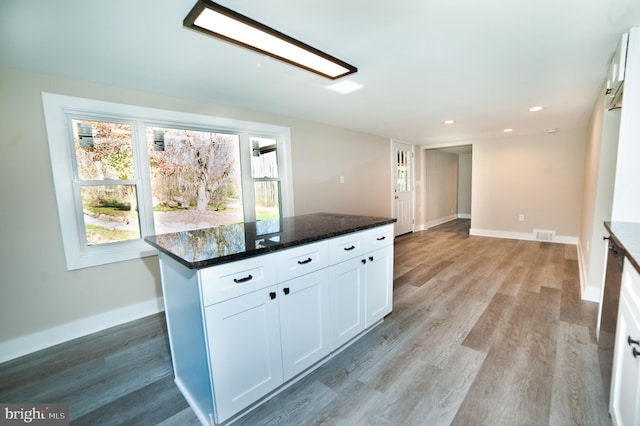 kitchen with dark stone countertops, white cabinetry, a center island, and light hardwood / wood-style floors