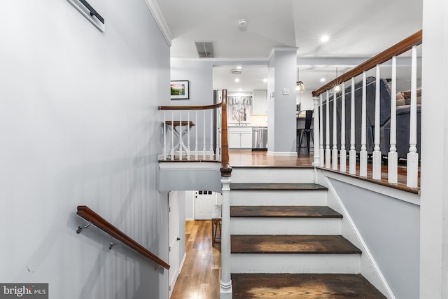 stairway with sink, wood-type flooring, and ornamental molding