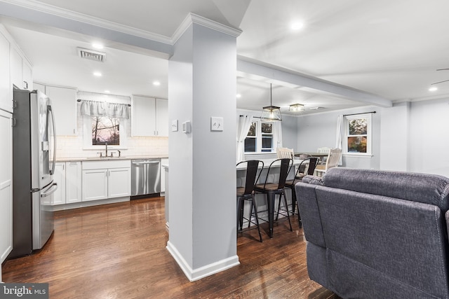 kitchen featuring dark hardwood / wood-style floors, ornamental molding, appliances with stainless steel finishes, tasteful backsplash, and white cabinetry