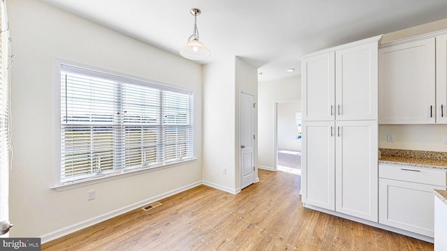 kitchen featuring white cabinets, pendant lighting, light stone countertops, and light hardwood / wood-style flooring