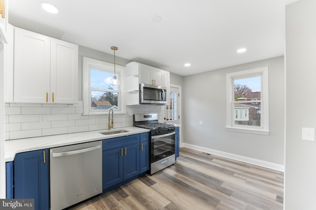 kitchen featuring stainless steel appliances, sink, blue cabinetry, light hardwood / wood-style flooring, and white cabinetry