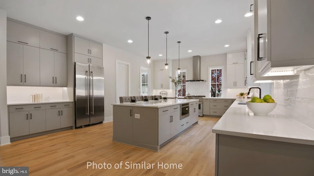 kitchen with premium appliances, decorative light fixtures, wall chimney range hood, a large island, and gray cabinetry