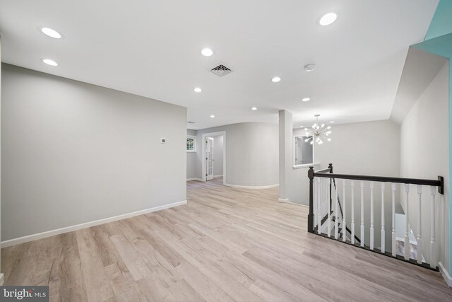 spare room featuring light wood-type flooring and an inviting chandelier