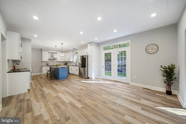 kitchen featuring pendant lighting, wall chimney range hood, stainless steel fridge, a kitchen island, and a breakfast bar area