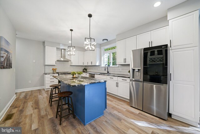 kitchen featuring a center island, wall chimney exhaust hood, stainless steel appliances, white cabinets, and light wood-type flooring