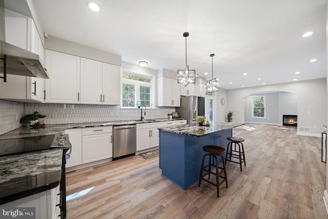 kitchen featuring white cabinetry, a healthy amount of sunlight, stainless steel appliances, dark stone countertops, and a kitchen island