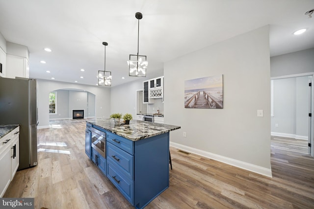 kitchen with blue cabinetry, light hardwood / wood-style flooring, dark stone countertops, stainless steel fridge, and white cabinets