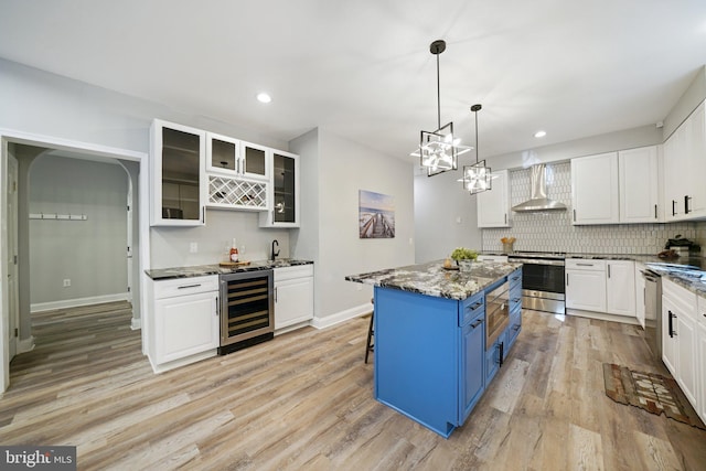 kitchen featuring wall chimney exhaust hood, blue cabinets, a kitchen island, light hardwood / wood-style flooring, and wine cooler