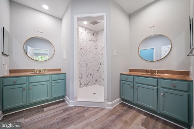 bathroom with a tile shower, vanity, and wood-type flooring