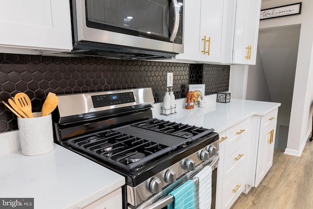 kitchen with tasteful backsplash, white cabinetry, appliances with stainless steel finishes, and light hardwood / wood-style flooring