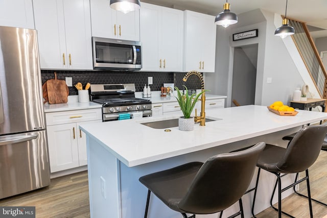 kitchen featuring white cabinetry, tasteful backsplash, an island with sink, decorative light fixtures, and appliances with stainless steel finishes